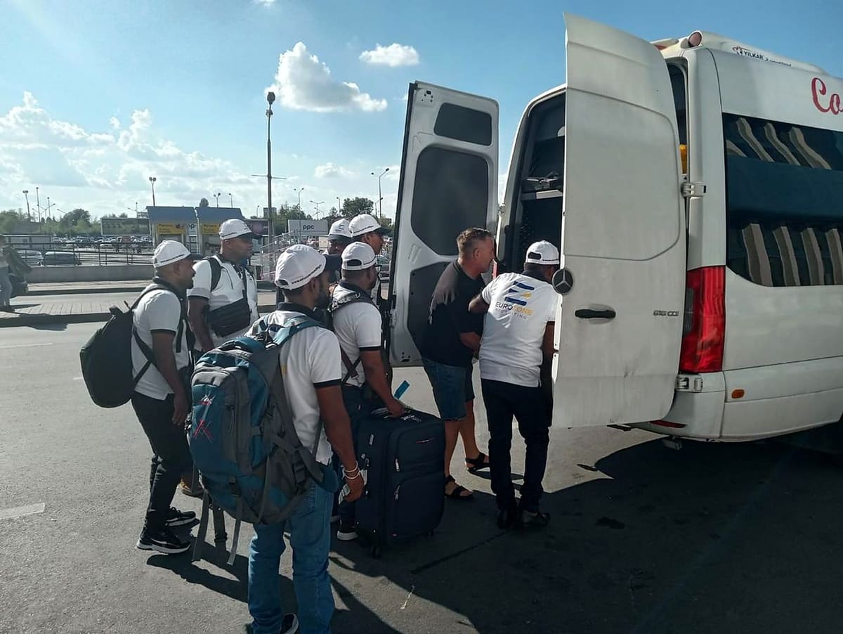 Eurozone workers in company polos and caps, with backpacks and a suitcase, loading their luggage into the pickup van outside the airport.