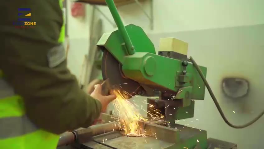 A worker in a hi-vis vest cutting a steel bar on a chop saw, sparks coming off the blade.